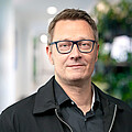 Dr. Lars Schwabe – Vice President Technology | CTO LHIND Mann mit kurzen grauen Haaren, grau umrandeter Brille, schwarzem Hemd und schwarzer Jacke
