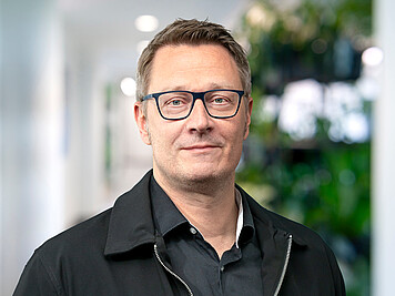 Dr. Lars Schwabe – Vice President Technology | CTO LHIND Mann mit kurzen grauen Haaren, grau umrandeter Brille, schwarzem Hemd und schwarzer Jacke