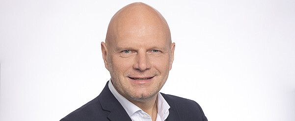 Freundlich lächelnder Mann mit Glatze, schwarzem Jackett und weißem Hemd